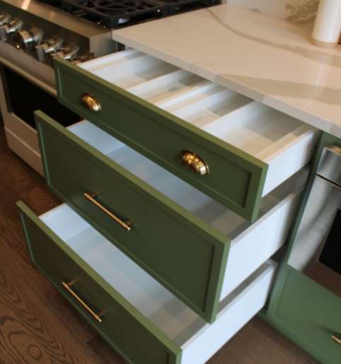 Functional green kitchen drawers with a built-in organizer, designed by a professional cabinet manufacturer.