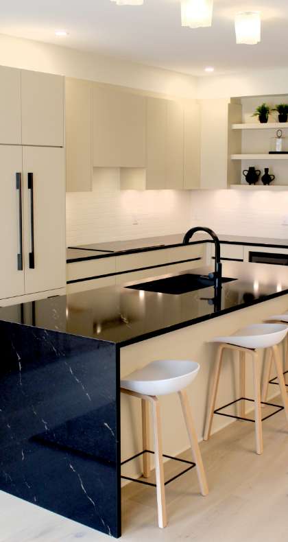 Minimalist beige custom kitchen cabinets with integrated appliances and a striking black marble island.